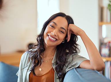 Woman smiling on couch at home, representing comfortable dental care and confident, healthy smile