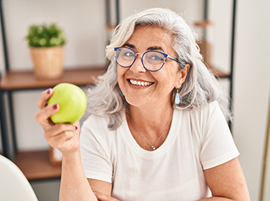 Older woman holding apple and smiling, representing preventive dental care and healthy lifestyle habits